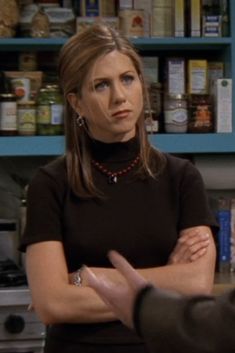 a woman standing in front of a counter with her arms crossed and looking at another person