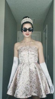 a woman wearing sunglasses and a tiara standing in a hallway with her hands on her hips