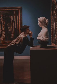 a woman looking at a busturine on display in a room with blue walls