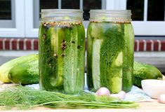 three jars filled with cucumbers sitting on top of a table next to onions