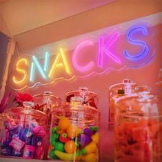 there is a neon sign on the wall above some jars with candies in them