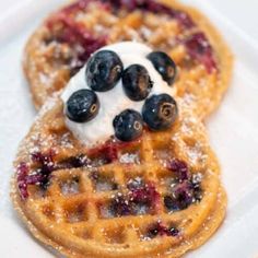 two waffles with blueberries and whipped cream on top are sitting on a white plate