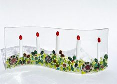 four white candles with red and green flowers on them in a clear glass display case