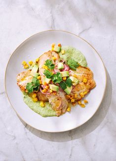 a white plate topped with meat covered in guacamole and garnish