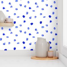 a white vase sitting on top of a counter next to a wall with blue spots