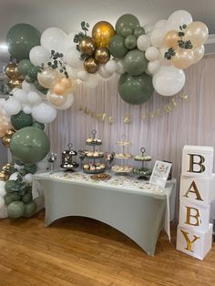 a table topped with lots of balloons next to a white and green cake stand on top of a hard wood floor