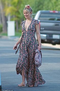 a woman is walking down the street in a floral dress and carrying a purse with her hand