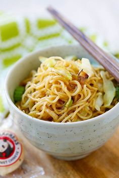 a bowl filled with noodles and vegetables next to chopsticks on top of a table