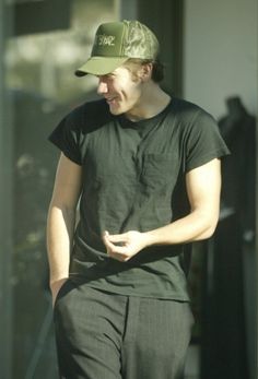 a man wearing a green hat and black shirt walking in front of a building with his hand on his hip