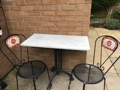 three chairs and a table in front of a brick wall with an orange flower design on it