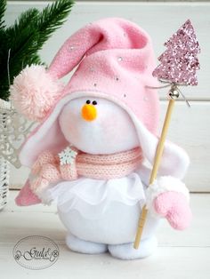 a stuffed snowman with a pink hat and scarf holding a sparkle wand in it's hand