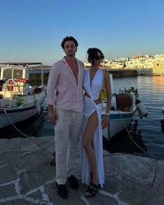 a man and woman standing next to each other in front of boats on the water