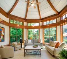 a living room filled with lots of furniture under a ceiling mounted fan and two large windows