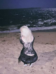 a woman is sitting on the beach with her back to the camera and looking at the water