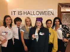 a group of women standing next to each other in front of a sign that says it is halloween