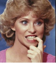 a close up of a person wearing a pink shirt and holding her hand to her chin