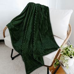 a green blanket sitting on top of a white couch next to a potted plant