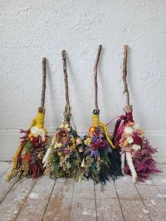 four brooms are lined up on the floor with flowers and feathers attached to them