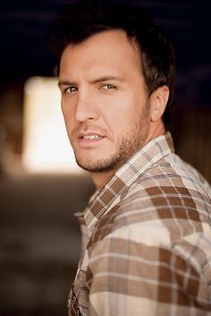 a close up of a person wearing a plaid shirt and looking at the camera with a serious look on his face