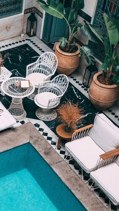 an outdoor patio with white wicker chairs and tables next to a swimming pool surrounded by potted plants