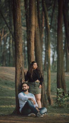 a man and woman sitting on the ground in front of some trees with their arms around each other