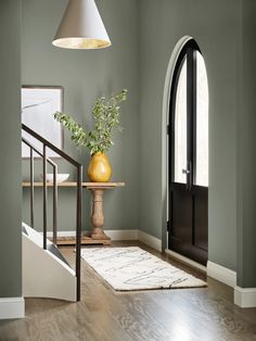 an entryway with green walls and wooden flooring, a yellow vase on a stand next to the door