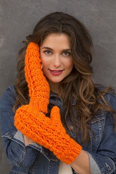 a woman wearing an orange crocheted mitten holding her hand up to the camera