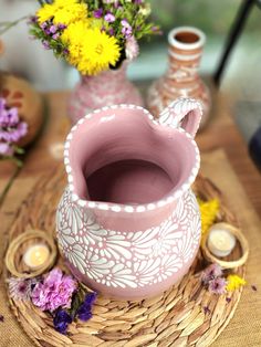 a pink vase sitting on top of a wooden table next to some yellow and purple flowers