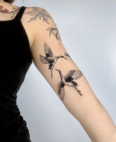 a woman's arm with tattoos on it and birds flying over the top of her arm