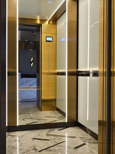 an elevator with marble flooring and gold door frames, leading to the entrance area