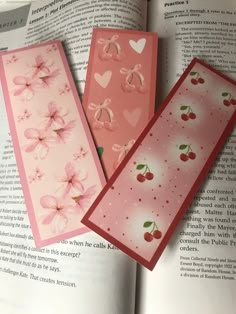 three bookmarks with cherry blossoms and hearts on them are sitting in an open book