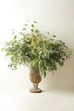 a vase filled with lots of greenery sitting on top of a white table next to a wall