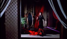 a woman standing in front of a mirror with red fabric on the floor next to it