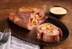 a black plate topped with meat and vegetables on top of a wooden table next to a fork