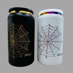 two black and white canisters with golden spider web designs on them, one is empty