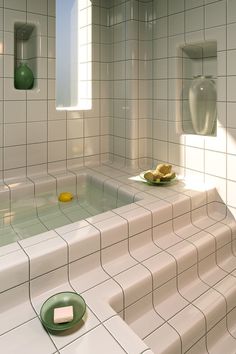 a white tiled bathroom with green plates on the floor and yellow objects in the bathtub