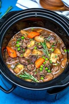 a crock pot filled with beef stew and carrots on top of a blue table