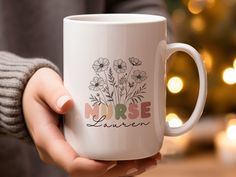 a person holding a white coffee mug with flowers on the inside and nurse written on it