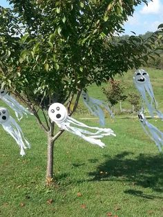 some white ghost decorations hanging from a tree in a field with green grass and trees