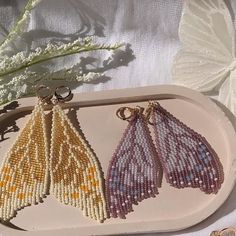 three beaded earrings sitting on top of a white tray next to a flower and butterfly