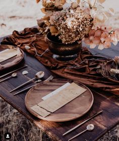 a wooden table topped with plates and utensils next to a vase filled with flowers