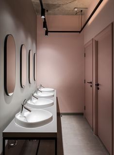 a row of sinks in a bathroom with mirrors on the wall and pink walls behind them