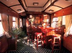 an old fashioned bar with stools in a room filled with wooden walls and windows