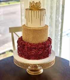 a three tiered cake with gold and red frosting on the top is sitting on a table