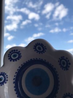 a blue and white plate sitting on top of a window sill with clouds in the background