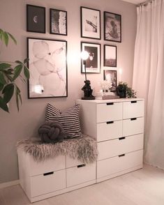 a white dresser sitting next to a window with pictures on the wall and a plant in front of it