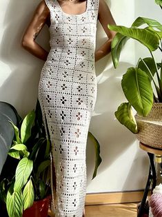 a woman in a white crochet dress standing next to a potted plant