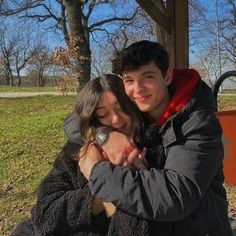 a man and woman hugging each other in front of a park bench on a sunny day