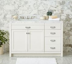 a bathroom with marble walls and flooring, including a white sink vanity topped with two plants