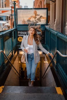 a woman is walking down the stairs with her hair blowing in the wind and holding a coffee cup